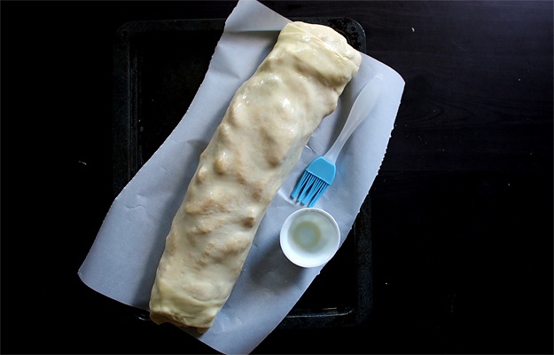 Apfelstrudel vor dem Backen mit Butter bestreichen